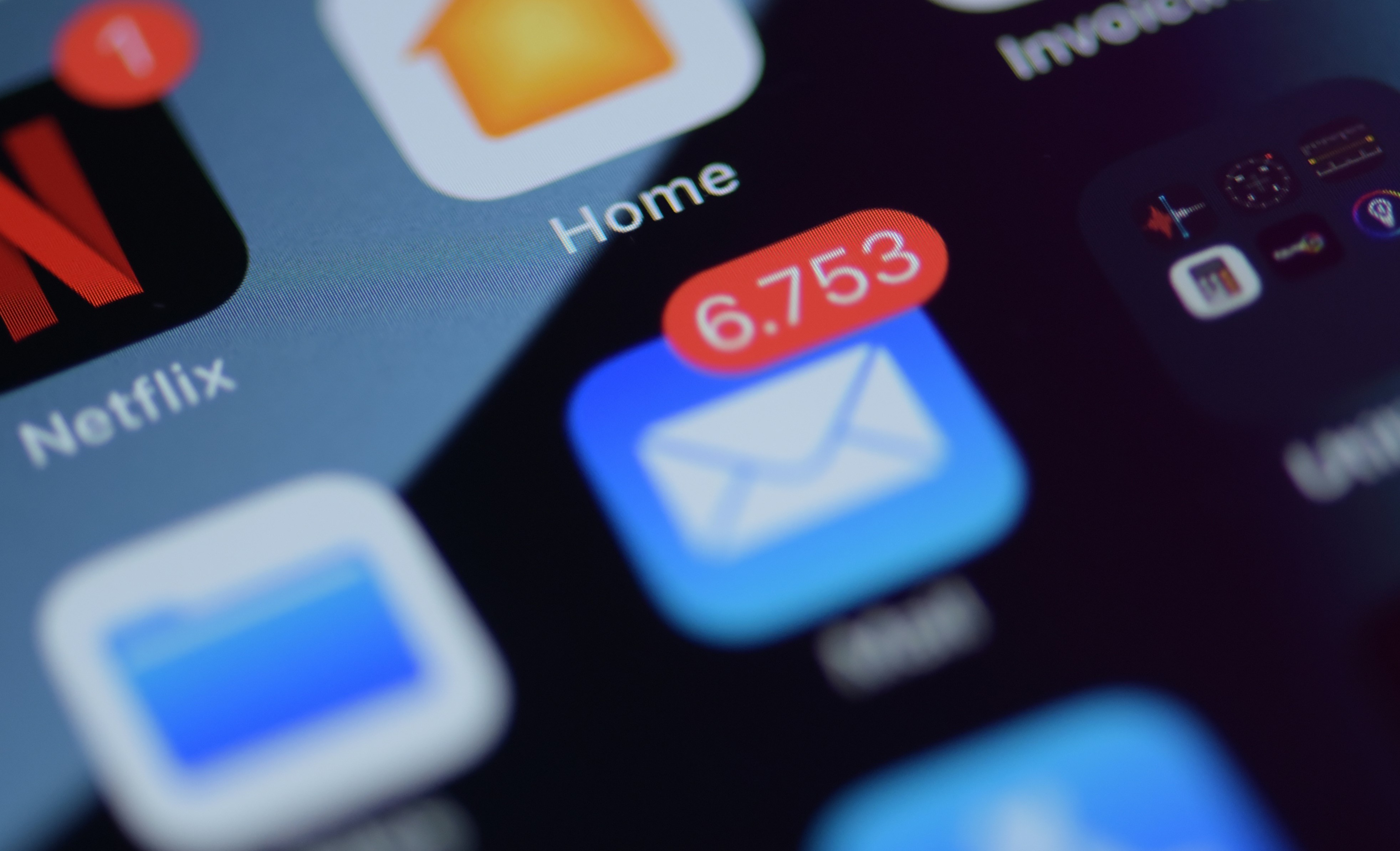 A close-up of an iPhone screen with the Mail app in the center, showing over 6,700 unread emails.
