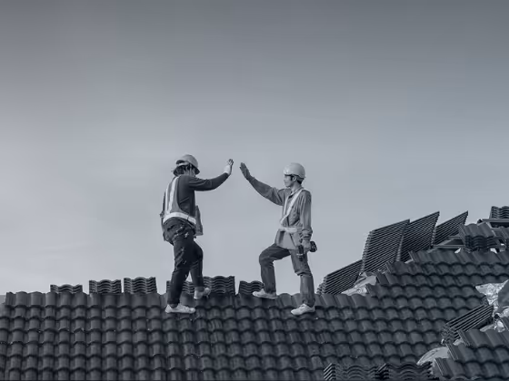 A black and white photo of two hardworking roofers high-fiving in front of a clear skyline.