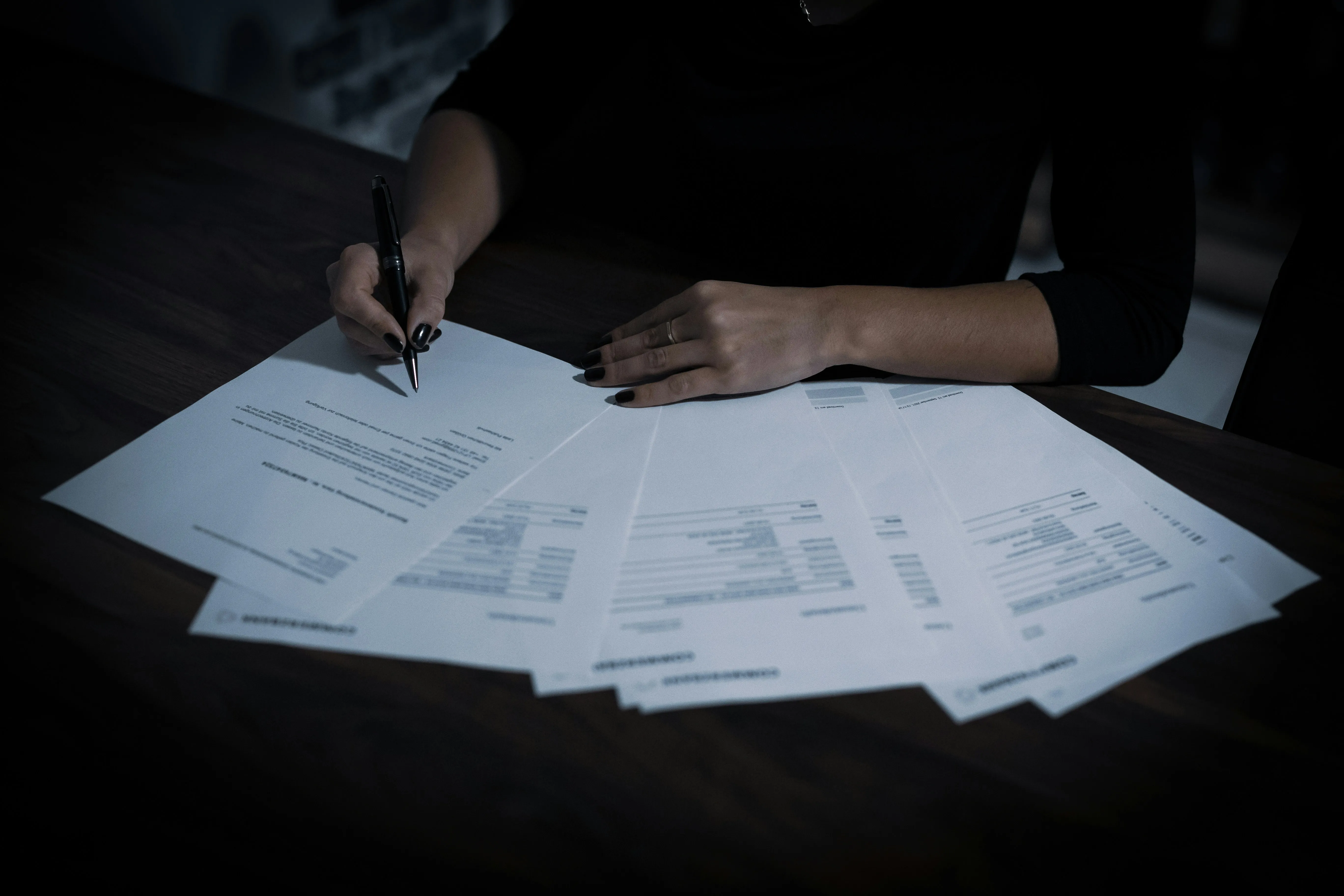 A photo of spread out pages with a woman's hands signing a roofing contract in a dark room.