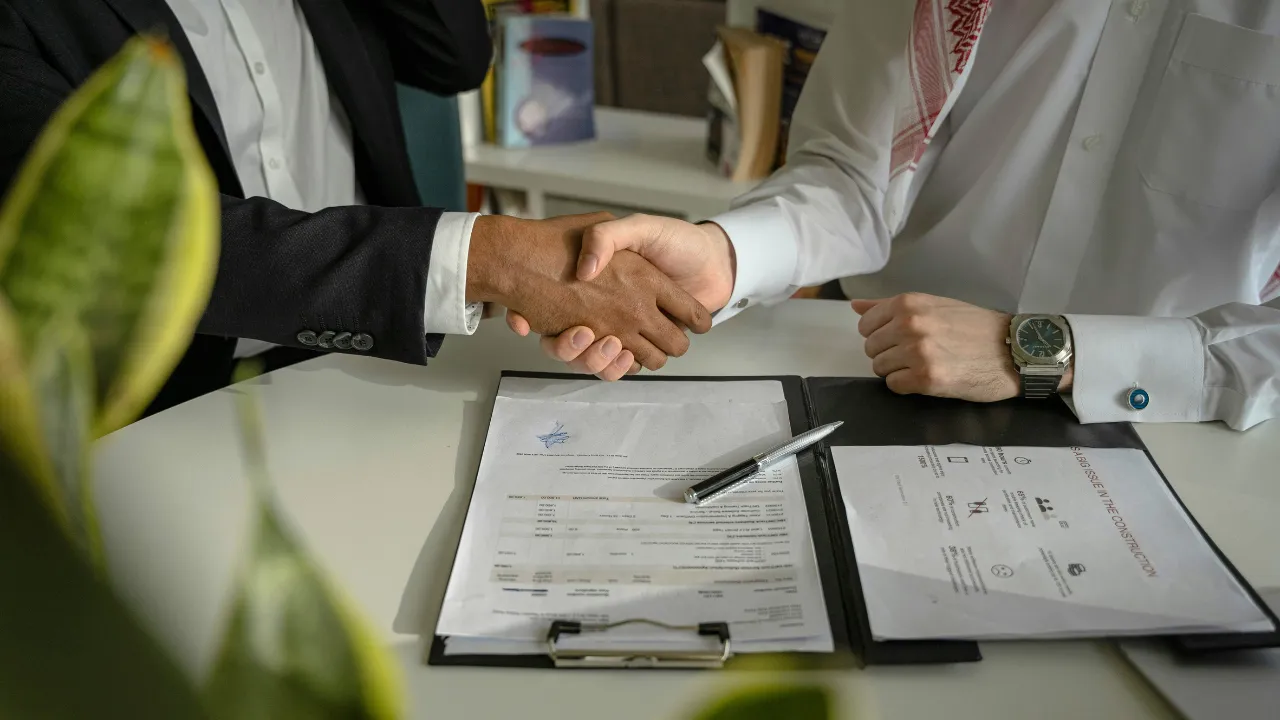 A professionally dressed roofer shaking hands with a homeowner after signing paperwork.