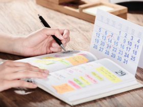 A photo of someone looking at a paper calendar and writing in a notebook, a process which roofing scheduling software replaces for roofing businesses.