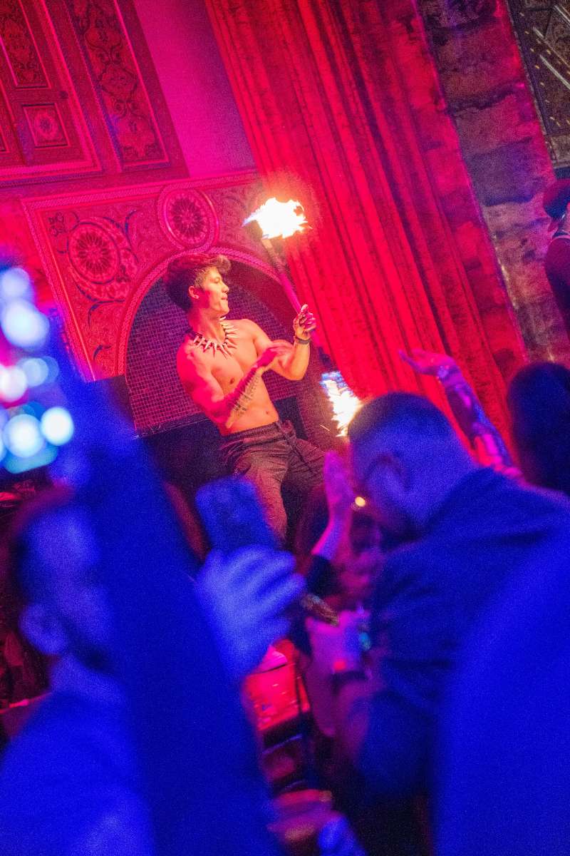 Luke Embers fire dancing on stage at indoor event.