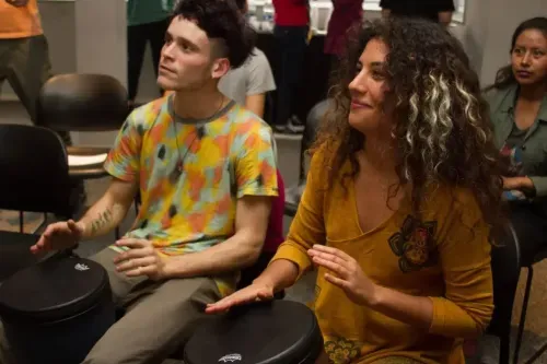 A man and a woman sitting next to each other, participating in Recreational drumming.