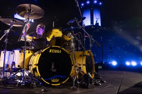 Metallica drummer Lars Ulrich play Remo drumheads on a bright yellow drum kit during a live Metallica concert under blue stage lights.