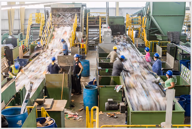 Recycling plant with workers sorting waste on conveyor belts.