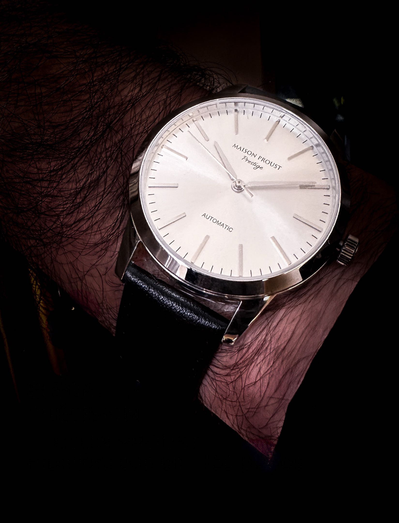 Close-up of a Maison Proust Prestige automatic wristwatch with a silver face and black leather strap.