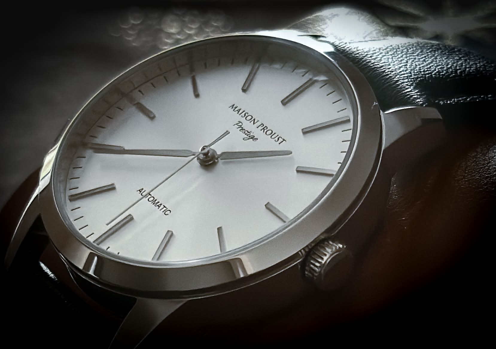 Close-up of a Maison Proust Prestige automatic wristwatch with a silver dial, minimalist hour markers, and black leather strap.