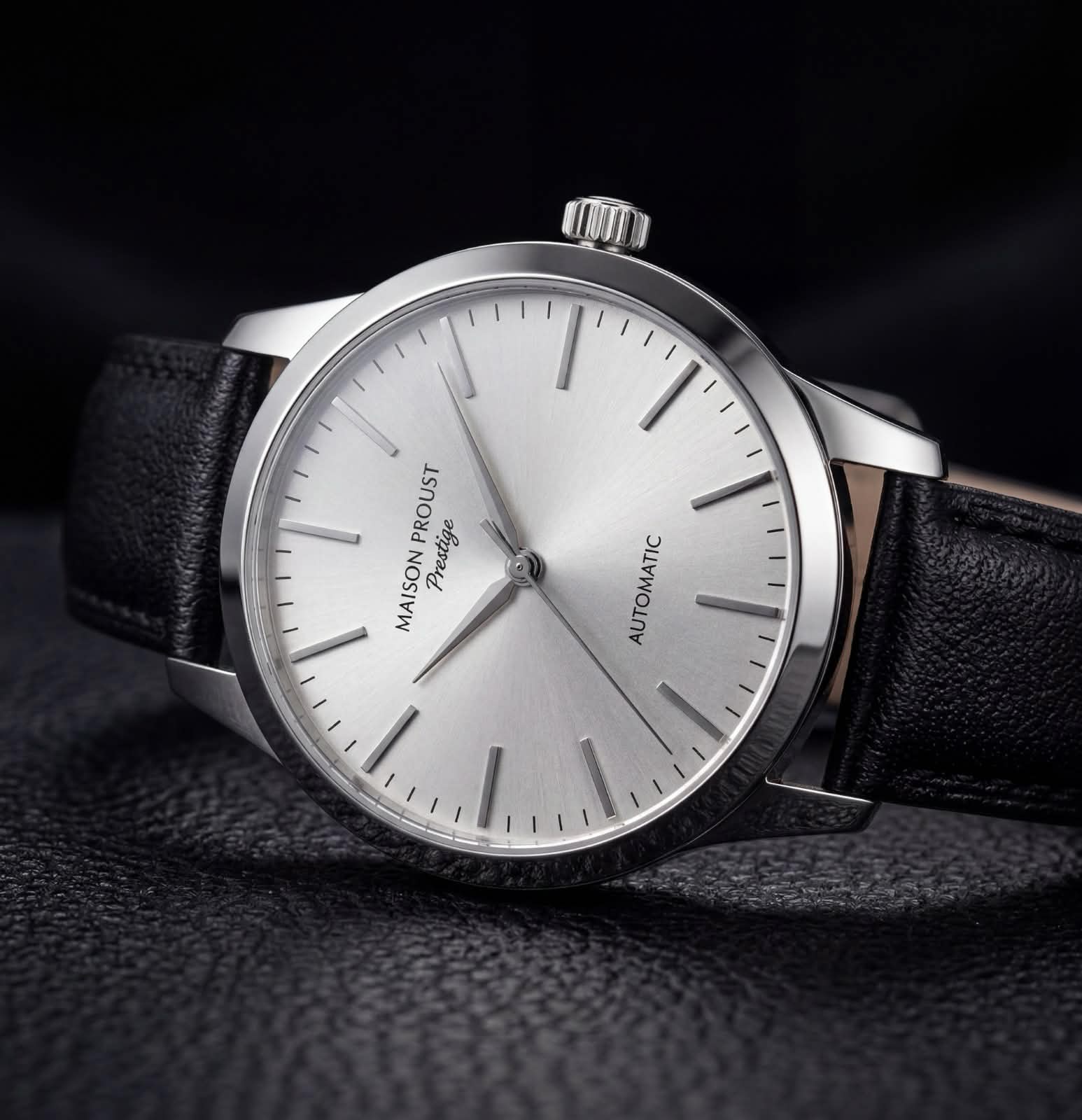 Montre automatique Maison Proust Prestige avec cadran argenté et bracelet en cuir noir sur fond noir texturé.