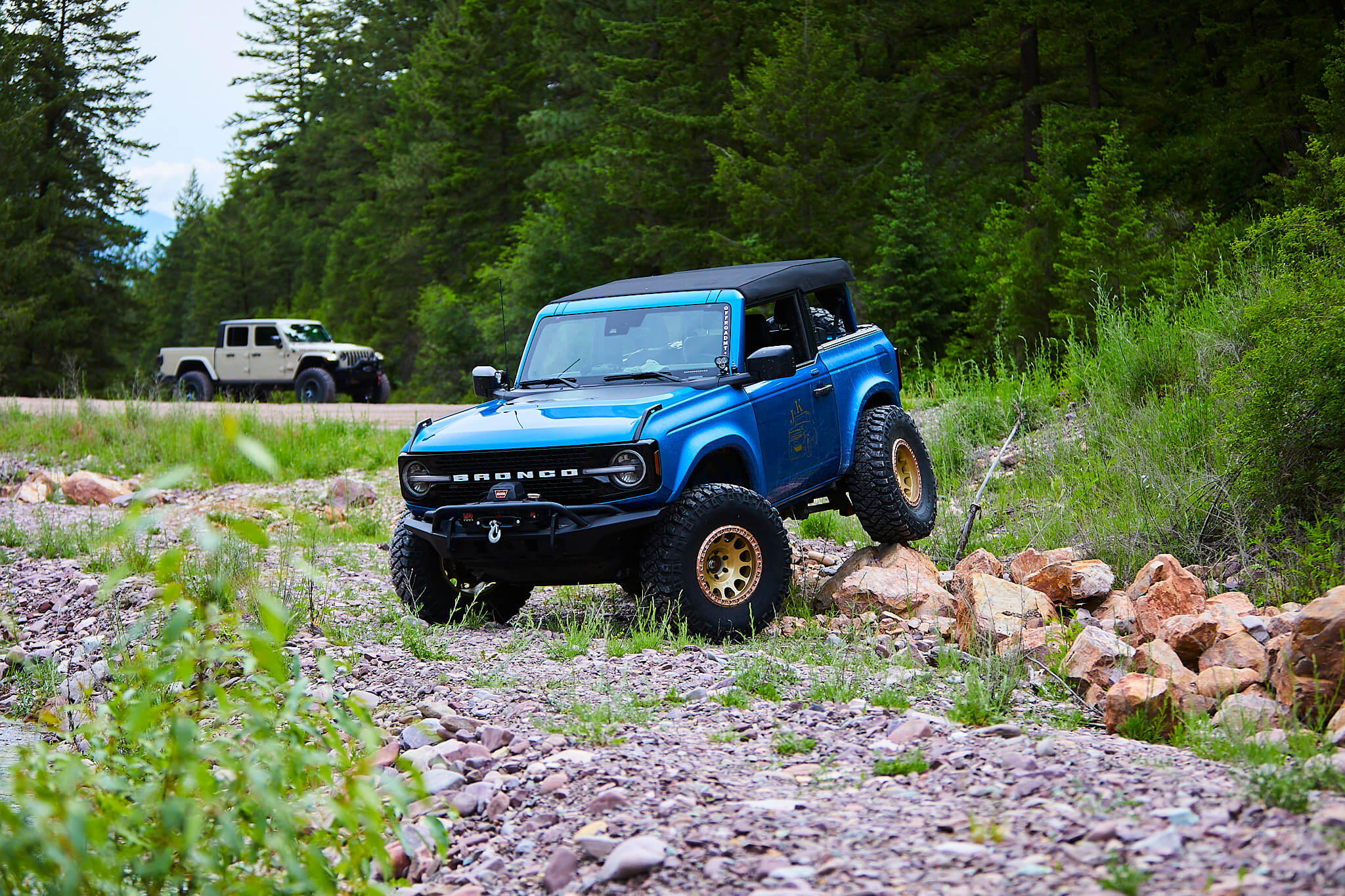 Ford Bronco parked on a rocky embankment with a jeep in the background.
