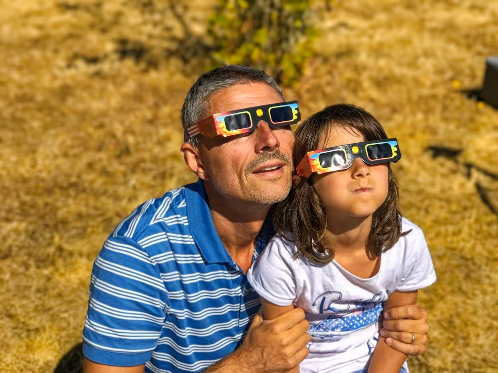 Man and daughter viewing solar eclipse with special glasses.