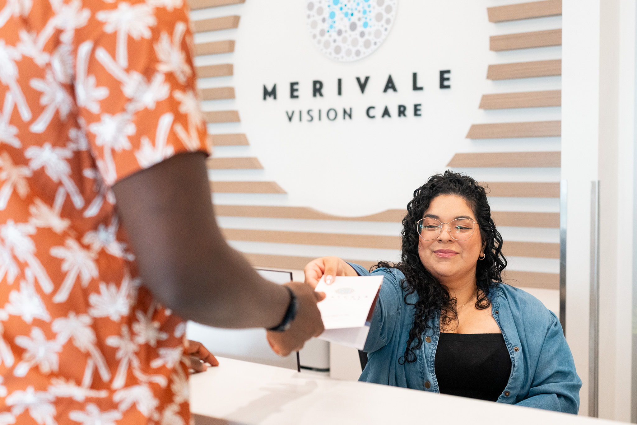 Front desk receptionist at Merivale Vision Care handing a client a pamphlet.