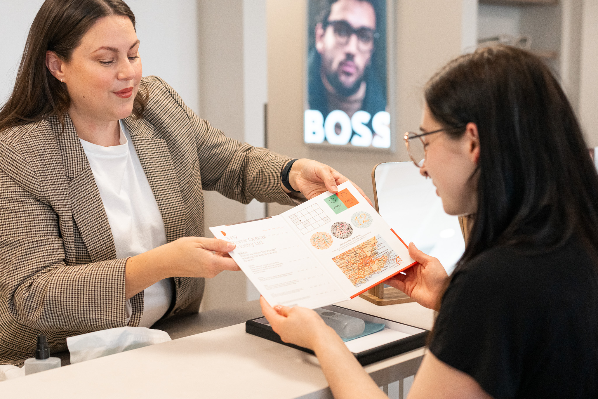 Optician showing a booklet to a patient; booklet covers eye issues such as colour blindness