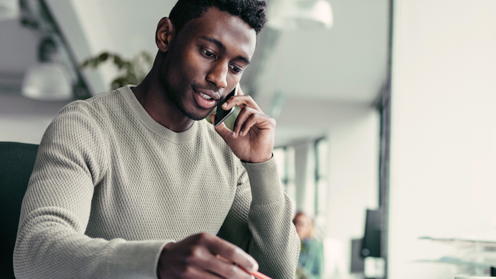 Young immigrant man talking on cell phone and writing notes