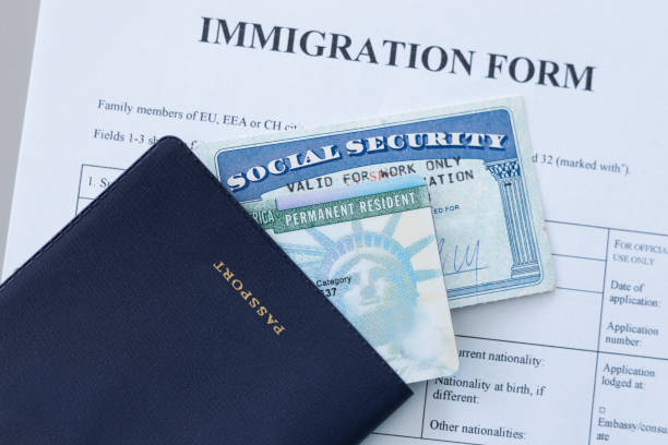 A dark passport, U.S. permanent resident card, and Social Security card resting on an official immigration application form.