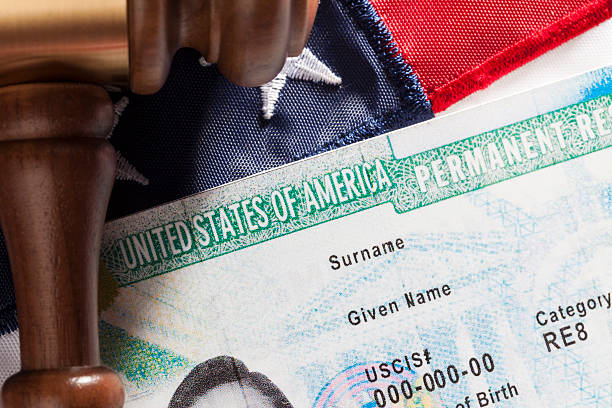 Close-up of a U.S. Permanent Resident card lying next to a wooden judge's gavel and an American flag.