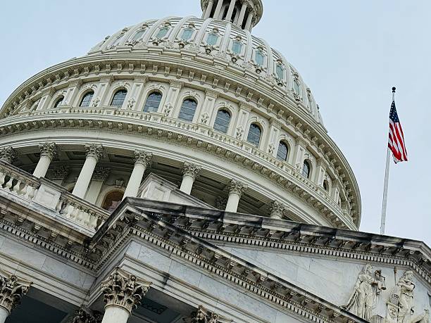 Low-angle shot of the U.S. Capitol Building dome with an American flag flying alongside it.