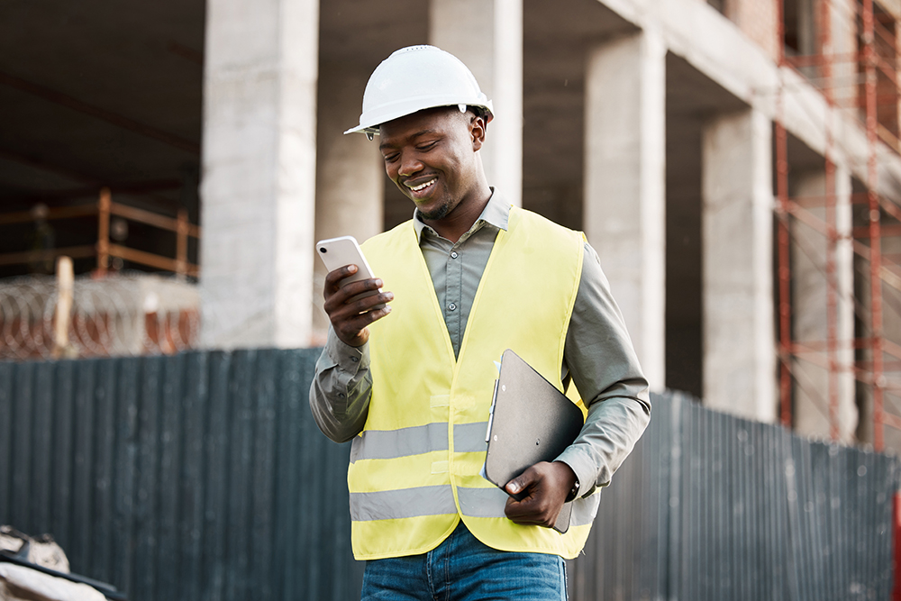 A construction worker on the job site looking at his phone and smiling