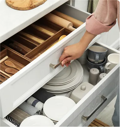 A person opening a white kitchen drawer filled with neatly organized plates and utensils.