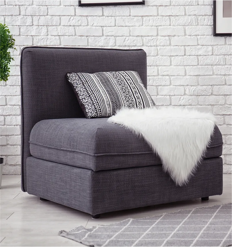 A modern dark gray armless chair with a patterned pillow and a white faux fur throw.