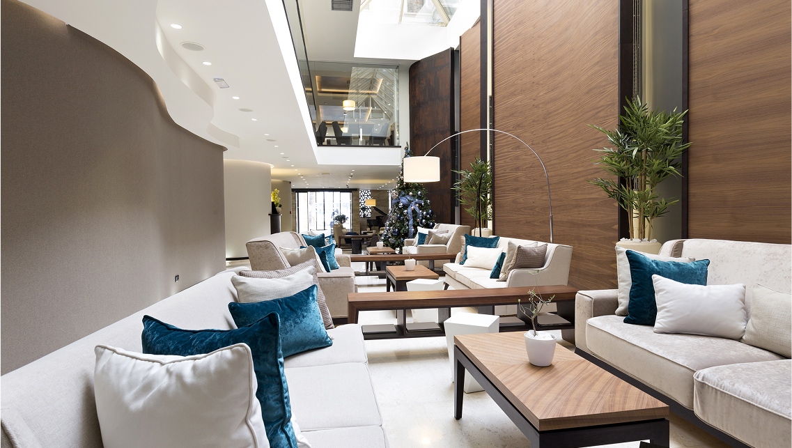 Spacious and modern hotel lobby or workplace lounge with white sofas and blue velvet cushions.
