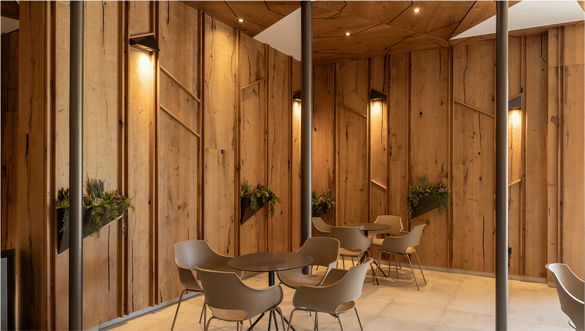 Modern cafe interior with geometric wood-paneled walls and ceiling, and several small tables with beige chairs.