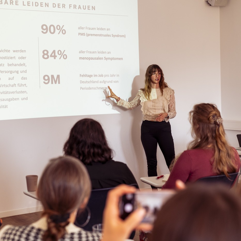 Frau, Beatrice Aretz, präsentiert vor Publikum Folien zu Frauengesundheit. Caona Health, Workshop, Zyklus, Frauengesundheit, Female Health, Female Empowerment.
