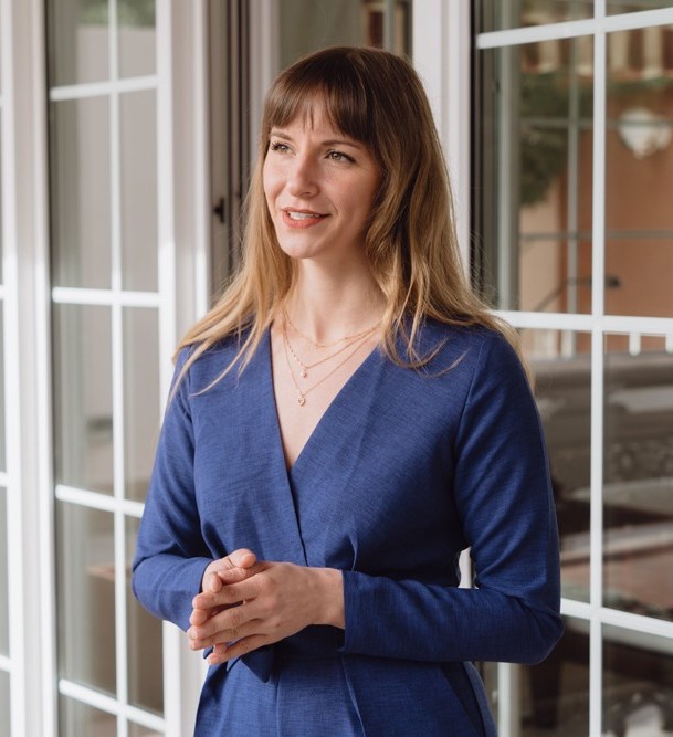 Frau, Beatrice Aretz, im blauen Business-Outfit spricht vor großen Fenstern. Caona Health, Keynote, Female Leadership, Female Empowerment, Femtech, Female Founder.