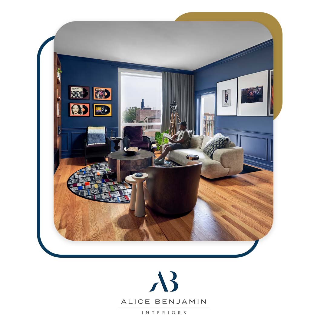 A person relaxing on a beige sofa in a modern living room featuring deep blue walls, hardwood floors, framed album art, and stylish contemporary furniture.