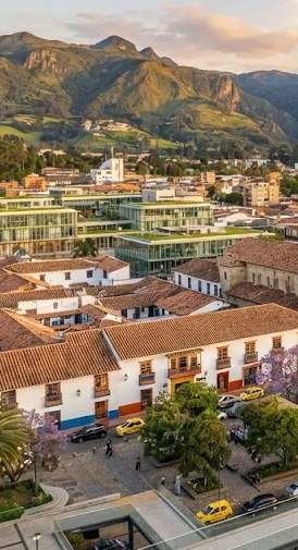 Vista aérea de edificio colonial y modernos con montañas verdes al fondo en un atardecer.