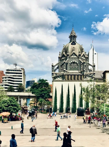 Plaza with people walking near a large historic building with a domed roof and tall trees during daytime.