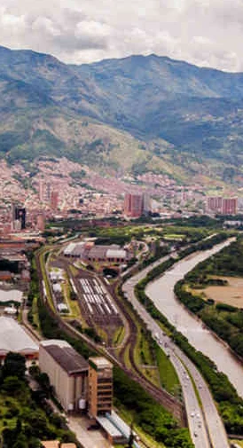 Ciudad entre montañas con río y carretera, edificios y zona verde visible en valle.