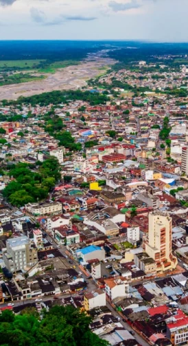 Vista aérea de la ciudad con edificios, calles y un río al fondo bajo un cielo parcialmente nublado.