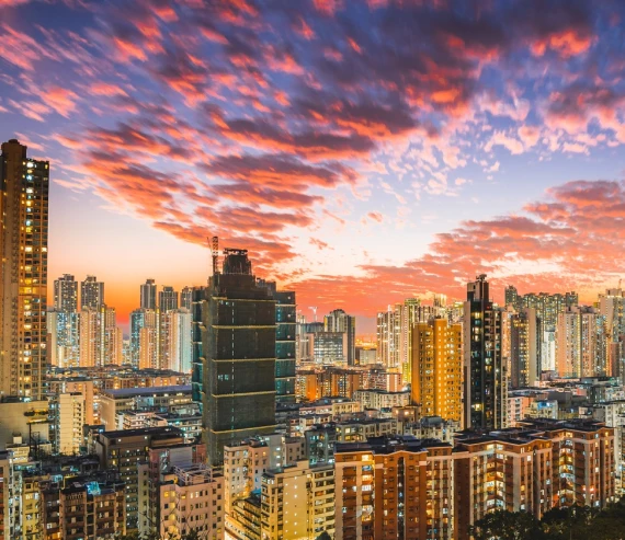Atardecer con nubes rosadas sobre una ciudad con muchos edificios altos iluminados.