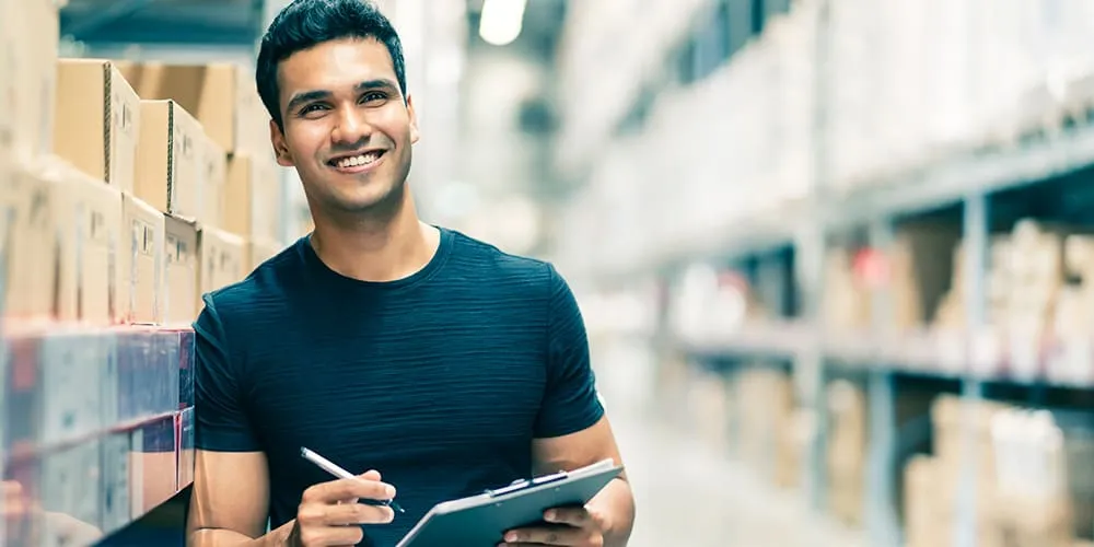 smart indian engineer man wearing safety helmet doing stock tick check cardboard stock product management factory warehouse background
