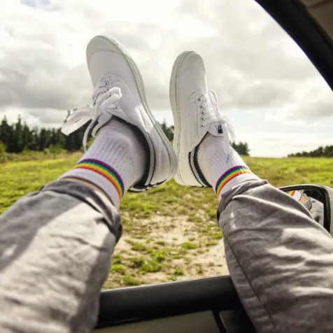 Beine mit Socken mit einem Regenbogen die aus dem Autofenster rausschauen.