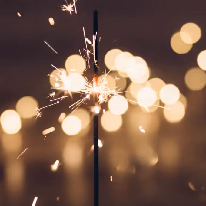 Close-up of a lit sparkler with glowing bokeh lights in the background, symbolizing New Year celebration and reflection.