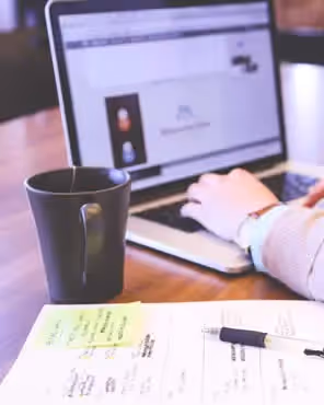Person working on a laptop with notes, pen, and coffee mug on desk, symbolizing top 5 email design tips for small businesses.