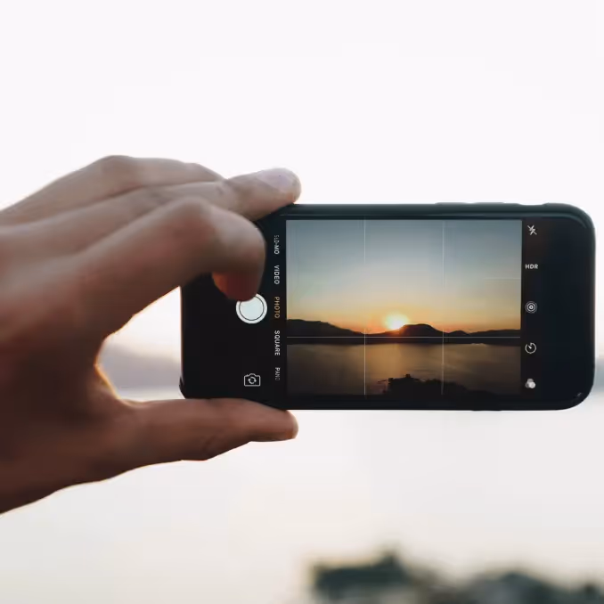 A hand holds a phone capturing a sunset, representing a tutorial on adding video content blocks in emails.
