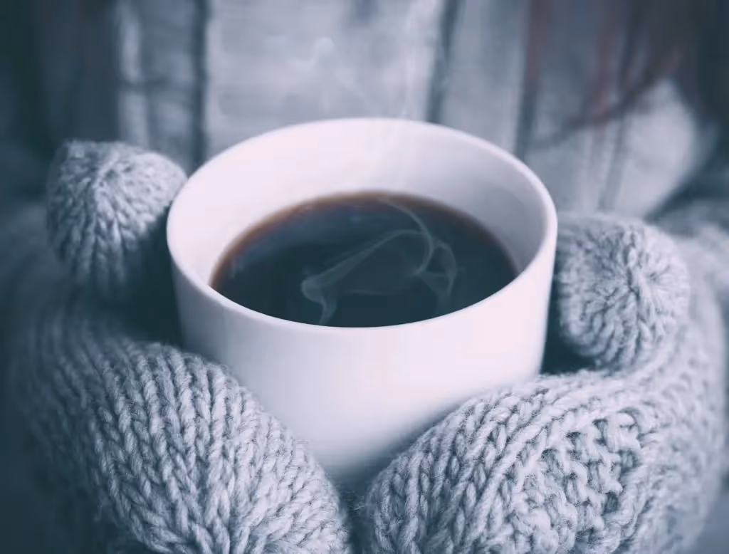 A warm cup of coffee held in cozy gray knit mittens, steam rising into the chilly air.