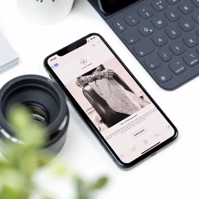 Smartphone showing a Blind Barber re-engagement email with black-and-white barber chair photo and a “COME BACK” button.