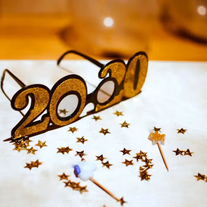 Gold glitter "2020" New Year party glasses on white surface with scattered gold stars and festive decor.