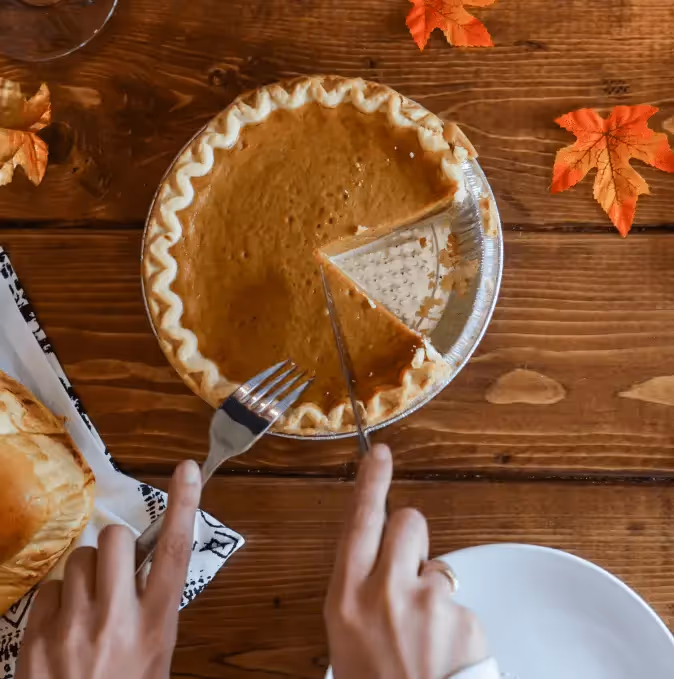 Thanksgiving email design concept with pumpkin pie, autumn leaves, bread rolls, and festive drink on a rustic wooden table setting.