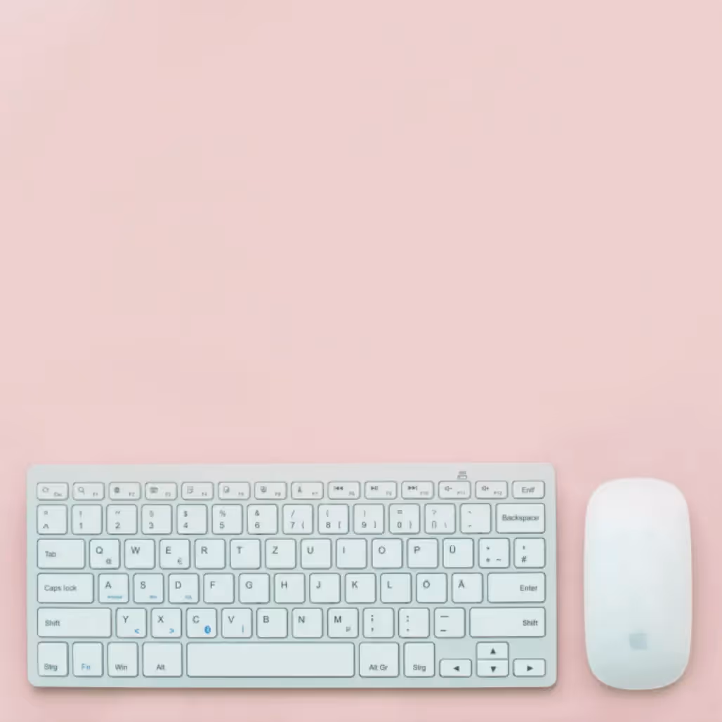 Minimalist flat lay with white keyboard and Apple mouse on pastel pink background, symbolizing clean and fresh spring email design.