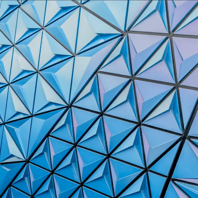 Architectural tessellation: Color-shifting 3D triangular panels in shades of blue and purple arranged in a repeating tessellated pattern on a modern facade