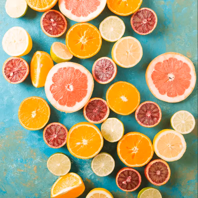 Flat lay of sliced citrus fruits—grapefruit, blood orange, orange, lime, and lemon—arranged on a turquoise surface.