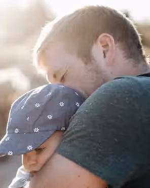 Father holding baby outdoors in warm sunlight, symbolizing love and bonding for Father's Day email inspiration.