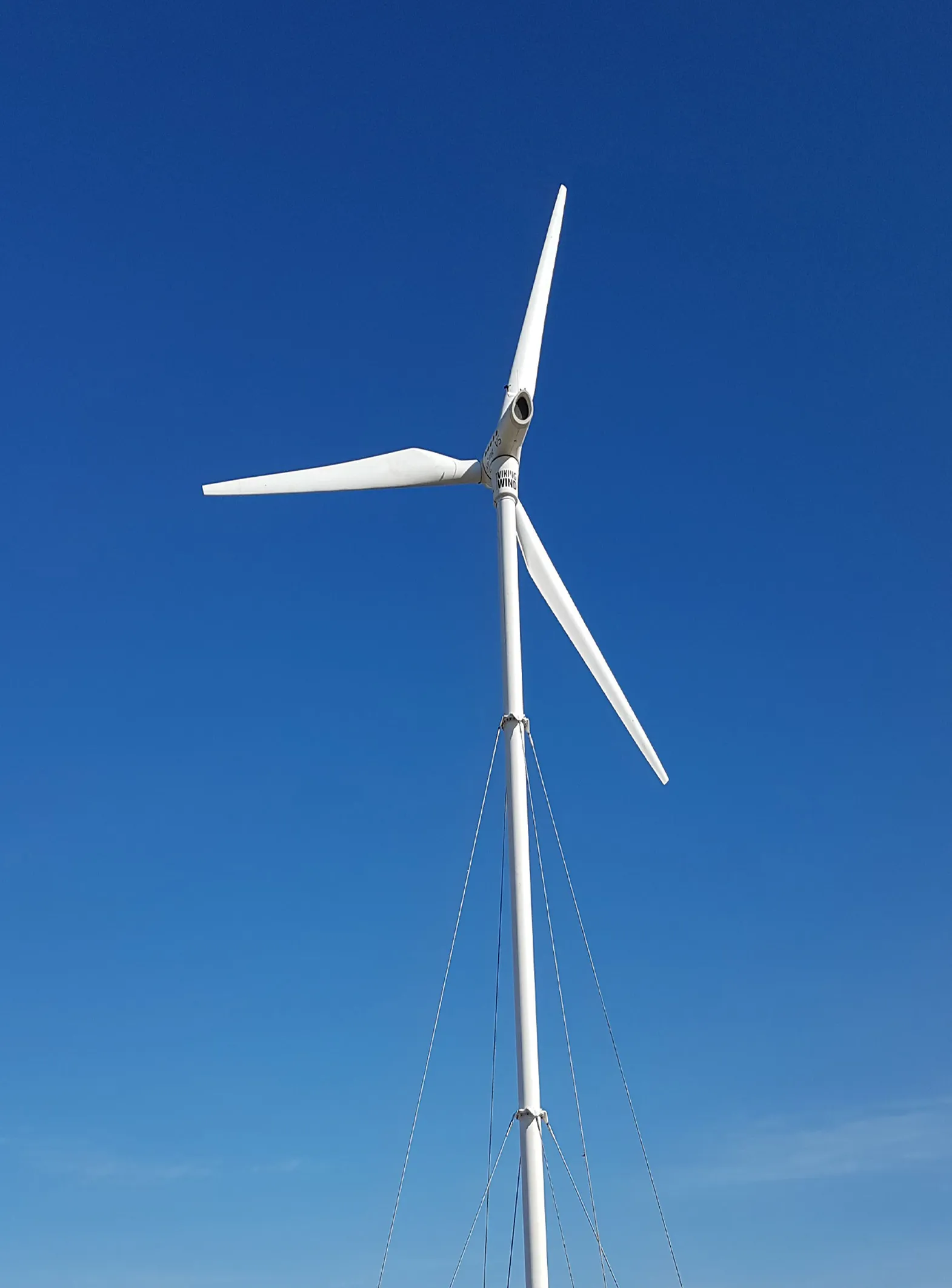 Weiße Windkraftanlage mit drei Flügeln vor strahlend blauem Himmel.