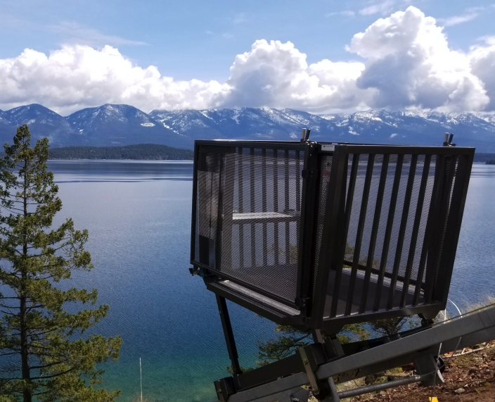 A tram on a steep hillside that goes down the hill to the lake and overlooks the lake and mountains.
