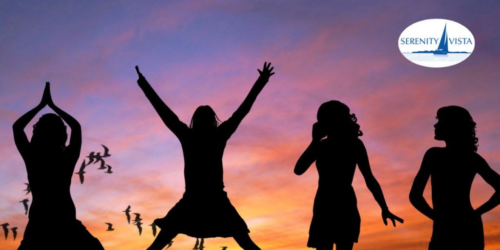 Four women celebrating together in silhouette against a colorful sunset