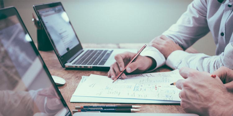 close-up of two computers with coworkers looking at handwritten notes containing the secrets of all human knowledge
